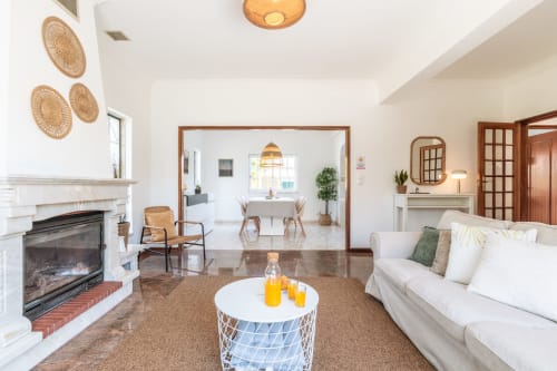 Sala luminosa com lareira, sofá branco, mesa de café tissida e área de jantar integrada na villa Amora
