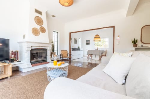 Sala de estar clara e integrada com lareira, móveis brancos e vista para o jardim na villa Arestas e Planetas perto de Caparica