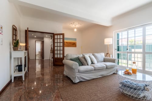 Elegante sala de estar em apartamento moderno com sofá bege, piso em azulejo escuro e portas de vidro com vista para o jardim em Arestas e
