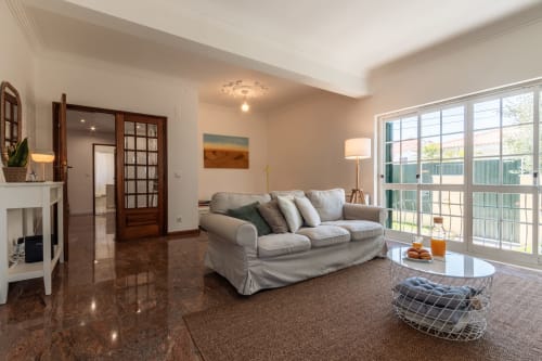 Sala de estar moderna com sofá cinzento, vista para o jardim e acesso ao terraço na villa Arestas e Planetas em Amora, Portugal