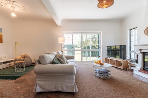 Sala de estar moderna com sofá bege, TV, lareira e vista para o jardim na villa Arestas e Planetas em Amora, Portugal