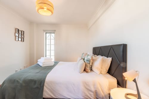 Quarto moderno com cabeceira escura, roupa de cama branca e luminária quente na villa Arestas e Planetas perto de Caparica, Portugal