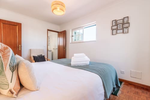 Quarto luminoso na villa Arestas e Planetas perto de Caparica, com cama branca, portas em madeira, janelas e comodidades modernas