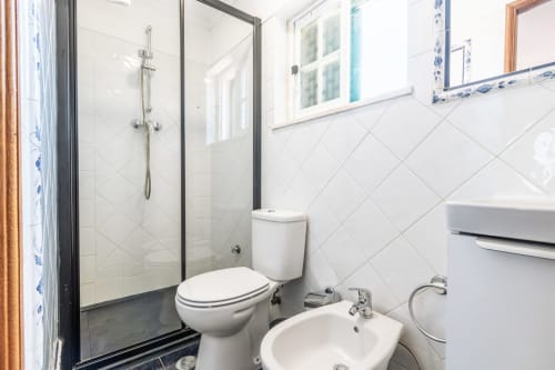 Banheiro moderno com azulejos brancos, box de vidro, vaso sanitário e pia no apartamento da villa Amora