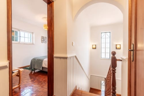 Escada e corredor luminosos com corrimãos de madeira na vila Arestas e Planetas, Amora, Portugal, com quarto visível ao fundo
