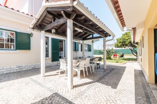 Pátio ensolarado com pérgola, cadeiras brancas e mesa de jantar na villa Arestas e Planetas em Amora, Portugal