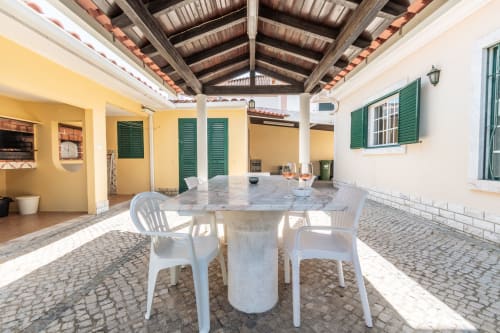 Terraço coberto com mesa e cadeiras de jantar brancas na vila Arestas e Planetas em Amora, Portugal