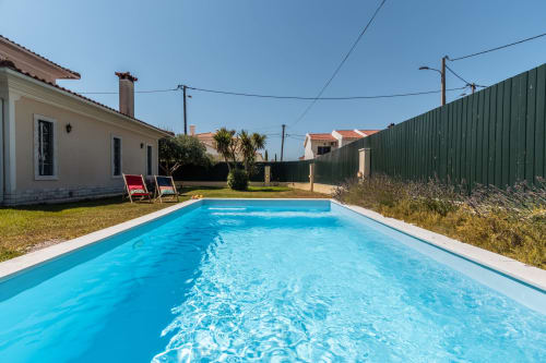 Vila com piscina privada em Amora, piscina azul brilhante, espreguiçadeiras, casa branca e cerca verde sob céu limpo