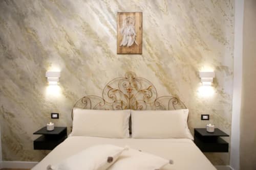 Camera da letto elegante alle Roma Imperial Suites con testata ornamentale, pareti in marmo, biancheria color crema e opera d'arte acchiappasogni.