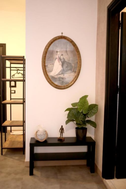 Elegante corridoio delle Roma Imperial Suites con consolle nera, pianta in vaso, ritratto ovale decorativo e scaffali in legno