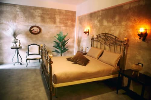 Camera da letto elegante presso Roma Imperial Suites con letto in ferro battuto, biancheria dorata, pareti in terracotta e illuminazione soft