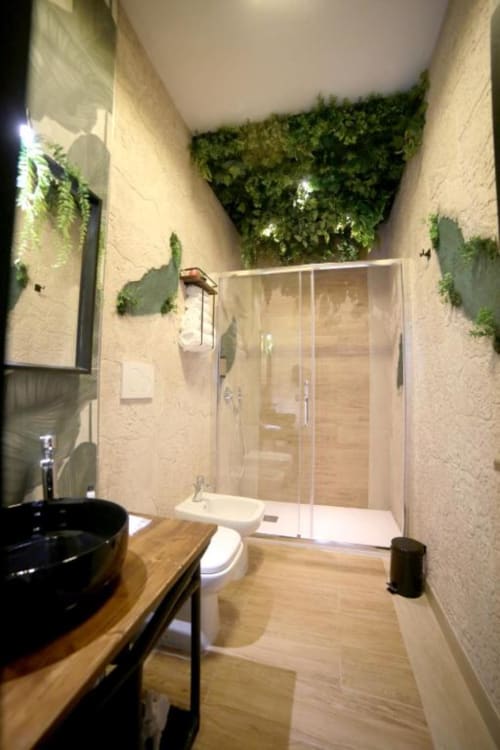 Bagno moderno con lavabo nero, ripiano in legno, box doccia in vetro e pareti verdi vive di Roma Imperial Suites