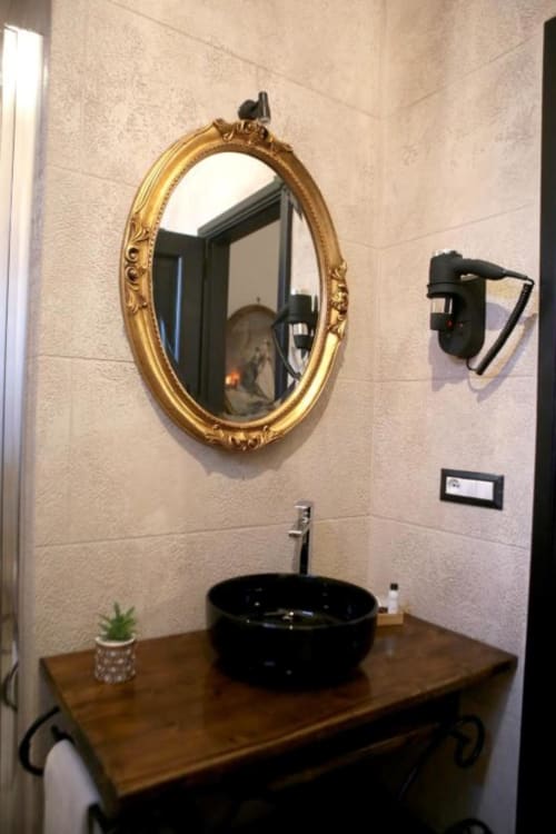 Lavabo moderno con ciotola nera, specchio ovale dorato e rivestimenti in ceramica presso Roma Imperial Suites