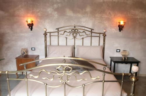 Camera da letto elegante alle Roma Imperial Suites con letto in ottone ornato, biancheria color crema, applique murale e arredamento italiano classico