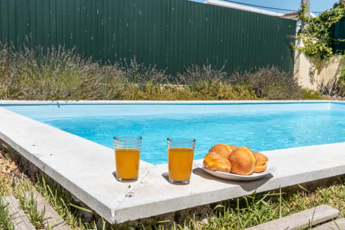 Piscina privada azul brilhante com bebidas douradas e pastelaria na varanda da villa Arestas e Planetas em Amora, Portugal