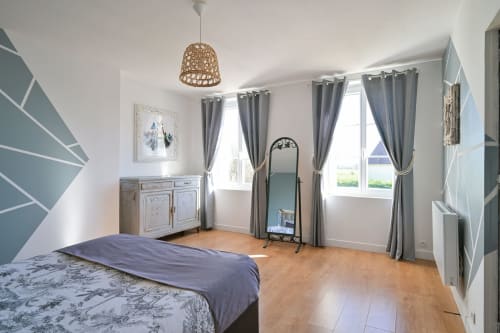 Helles Schlafzimmer in der Villa Ziane nahe Étretat mit Holzboden, Gartenblick, grauen Vorhängen und geometrischer Akzentwand