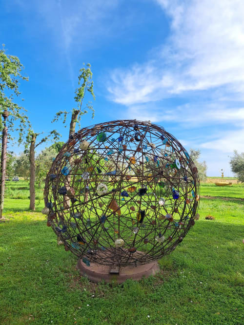 Metal sphere sculpture with colorful elements on green lawn at Agriturismo La Tortorella, Grosseto, Italy