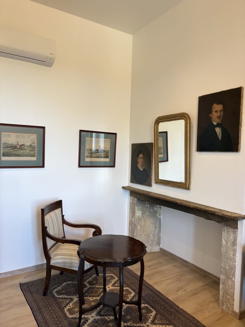 Élégant salon du gîte Le Montreal à Montréal du Gers : fauteuil ancien, table ronde, cheminée et portraits d'époque