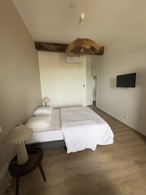 Chambre moderne au gîte Le Montreal à Montréal du Gers avec literie blanche, poutre en bois, luminaire suspendu et TV murale