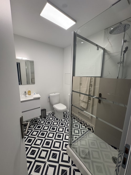Salle de bain moderne au Le Montreal B&B à Montréal du Gers avec carrelage géométrique, douche à l'italienne, toilettes et vasque.