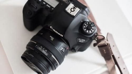 Appareil photo Canon EOS 6D avec objectif 70mm et sangle marron sur surface blanche à l'Ô Château hotel à Hayange