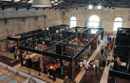 Padiglioni neri riempiono lo spazio di un magazzino industriale all'evento Ca Cortigiane di Venezia con visitatori che consultano gli espositori