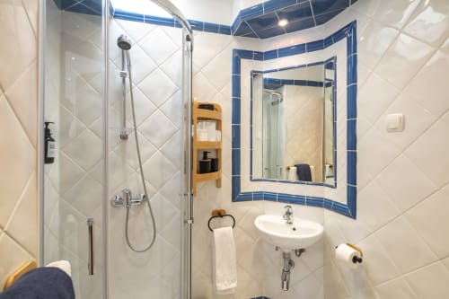 Banheiro moderno com azulejos brancos, espelho com moldura azul, pia suspensa e box de vidro na Casa Mac, Carvoeiro