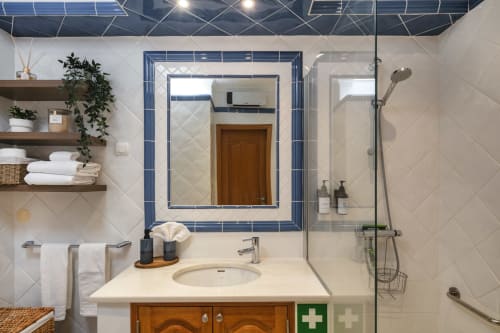 Banheiro moderno com espelho de moldura azul, pia branca, gabinete em madeira, chuveiro walk-in e prateleiras flutuantes na Casa Mac