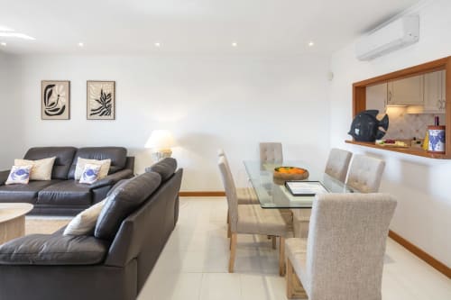 Sala de estar e jantar moderna no apartamento Casa Mac, Carvoeiro, com sofá de couro preto, mesa de jantar em madeira e cozinha