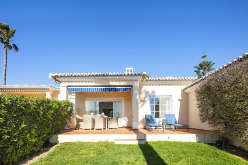 Terraço do apartamento Casa Mac em Carvoeiro com espreguiçadeiras azuis, jardim bem cuidado e arquitetura mediterrânea