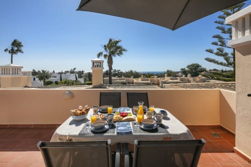Rooftop terrace breakfast setup at MarVillas Rentals in Lagoa with ocean views, palm trees, and Mediterranean architecture