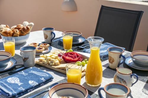 Bright breakfast table set with croissants, cheese, fruit, orange juice, and blue patterned dishware at MarVillas Rentals in