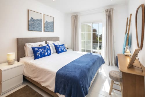 Modern bedroom at MarVillas Rentals in Lagoa with blue accents, white linens, coastal artwork, and balcony views