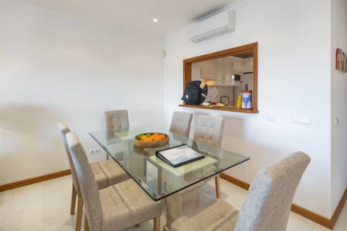 Modern dining area in MarVillas Rentals, Lagoa, with glass table, upholstered chairs, and open kitchen view
