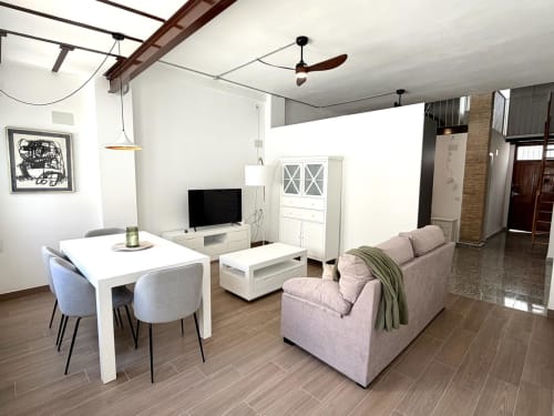 Loft urbano moderno en Valencia con mesa de comedor, sofá rosa, televisión, cocina y piso de madera