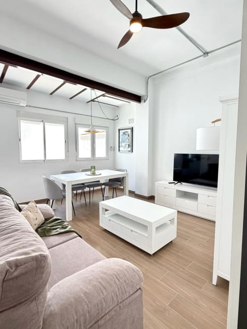 Salón moderno de apartamento en Valencia con sofá, televisor, mesa de comedor, ventilador de techo y vistas a la ciudad