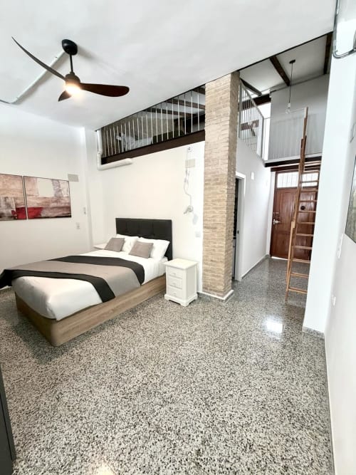 Moderno loft dormitorio en Valencia con cama, ventilador de techo, altillo, pared de ladrillo y vistas a la ciudad en Stay Gest