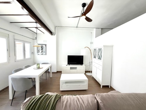 Sala de estar moderna en loft de Valencia con comedor, televisión, muebles blancos, ventilador de techo y vistas a la ciudad