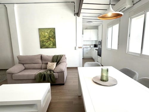 Área de estar de un loft moderno en Valencia con sofá gris, mesa de comedor, cocina y vistas a la ciudad