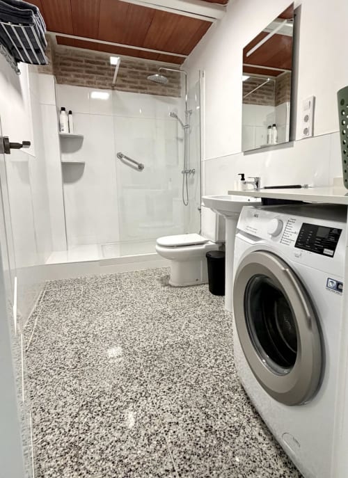 Moderno cuarto de baño en apartamento de Valencia con ducha, inodoro, lavamanos, lavadora y suelo de baldosas moteadas