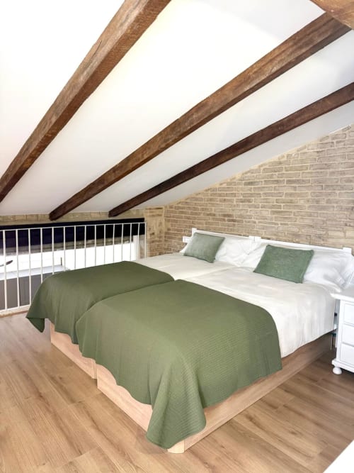 Dormitorio loft moderno con vigas de madera vista, paredes de ladrillo y cama de matrimonio con ropa de cama verde en Stay Gest Valencia