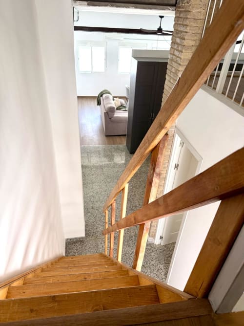 Escalera de madera con barandilla marrón que desciende a la sala de estar amueblada de un moderno apartamento en Valencia