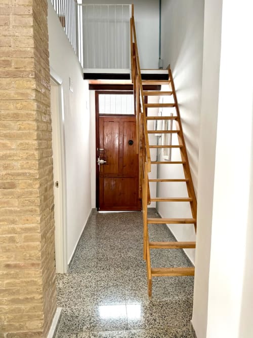 Pasillo estrecho con escalera de madera hacia el nivel superior, pared de ladrillo y puerta de madera en apartamento Stay Gest Valencia
