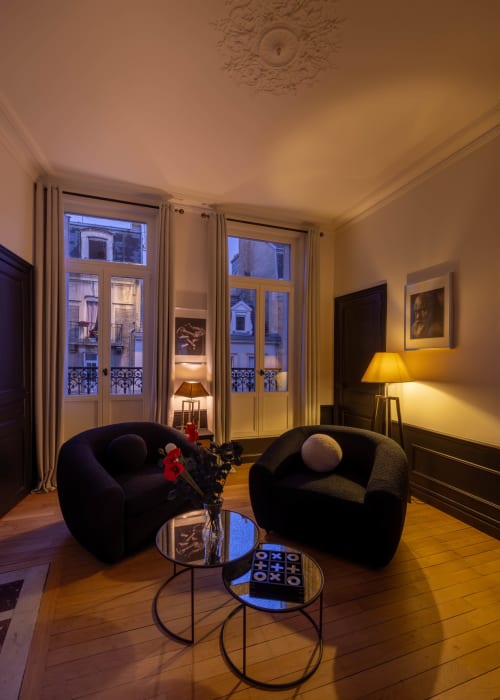 Elegant Parisian apartment living room with two black curved armchairs, Haussmann-style French doors overlooking Epernay