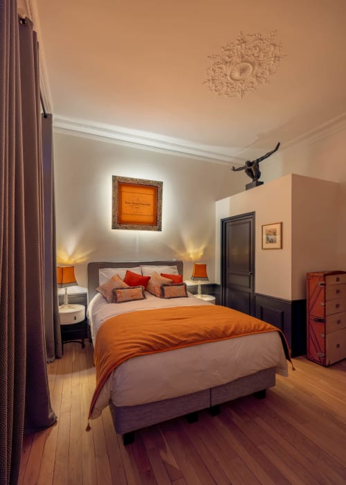 Elegant bedroom at Secrets de Chef de Cave in Epernay with orange accents, ambient lighting, and wooden flooring