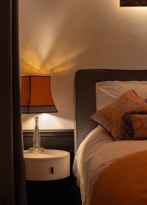 Luxury bedroom at Secrets de Chef de Cave, Epernay, with orange lamp, patterned pillows, and warm ambient lighting
