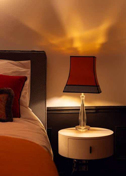 Elegant bedside lamp on round nightstand in Epernay hotel room with warm golden sunset lighting