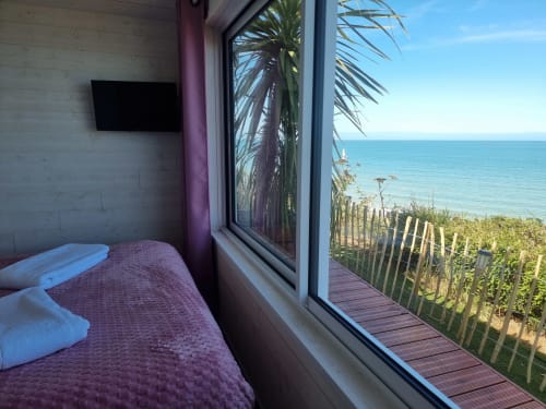 Chambre du cottage La Mer à Bayeuzen avec vue sur mer, palmier, terrasse en bois et TV écran plat à Saint-Côme-de-Fresné