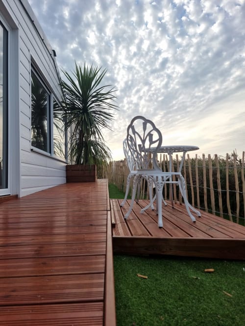 Chaise blanche ornementale sur la terrasse en bois du gîte Bayeuzen, Saint-Côme-de-Fresné, avec vue sur mer et plante palmier