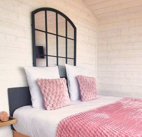Chambre douillette du cottage Bayeuzen avec coussins rose texturés, literie blanche et tête de lit arquée à cadre noir